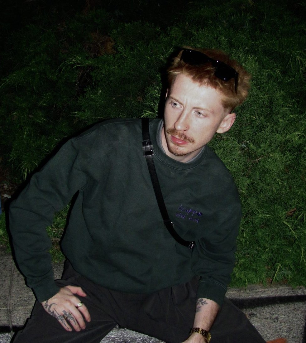 Václav crouching at night in a green sweater, lit by a camera flash