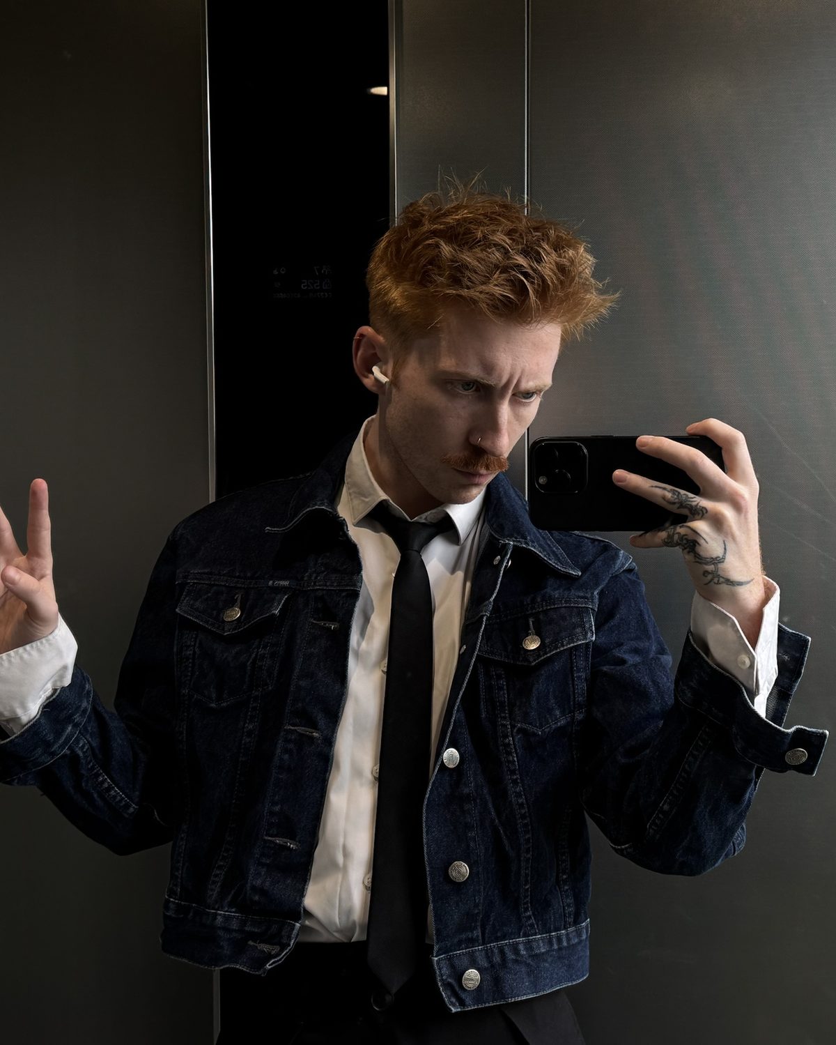 Václav in a denim jacket and tie, throwing a peace sign in a mirror selfie