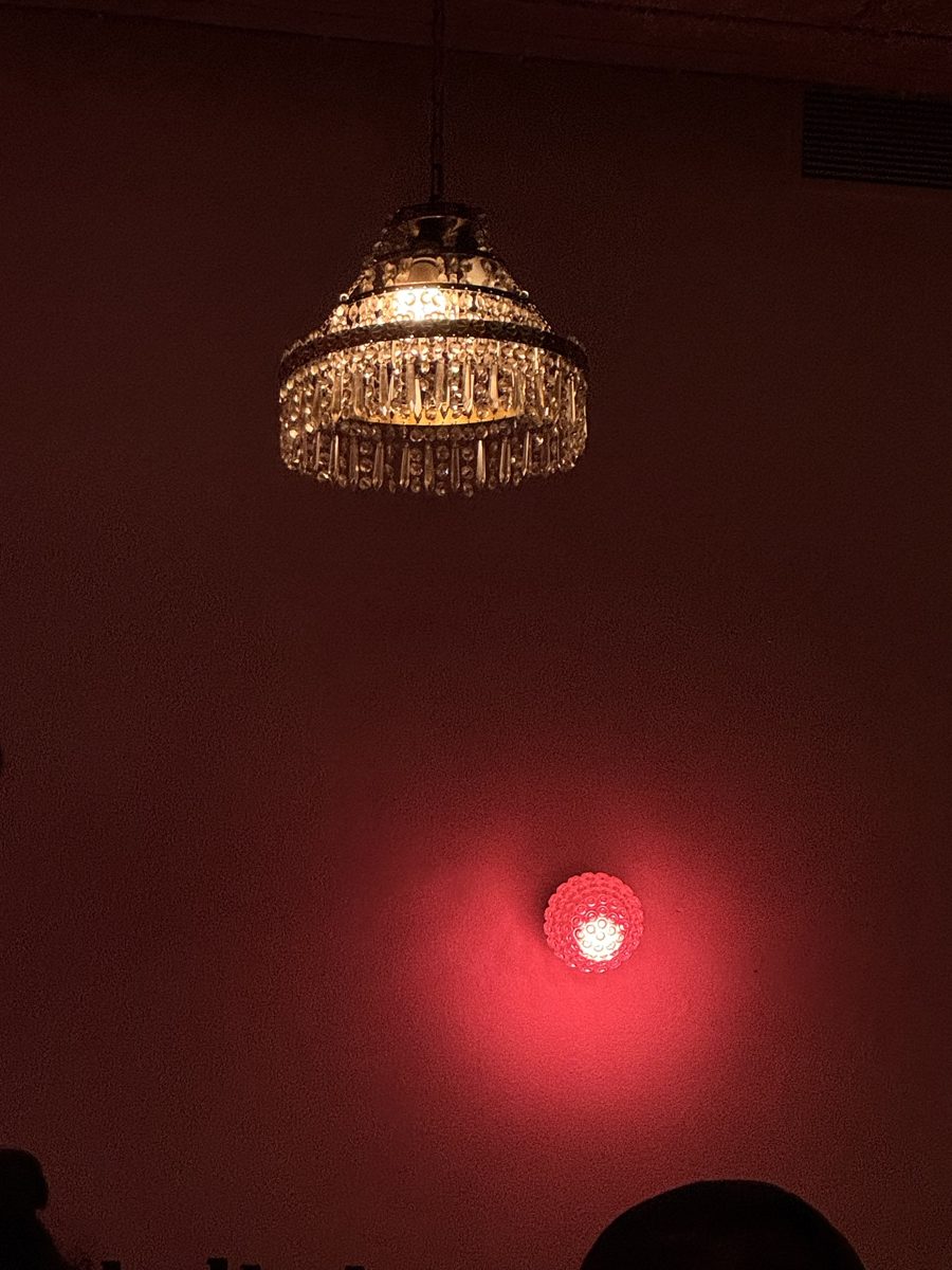 A crystal chandelier and a red wall light in a dark room