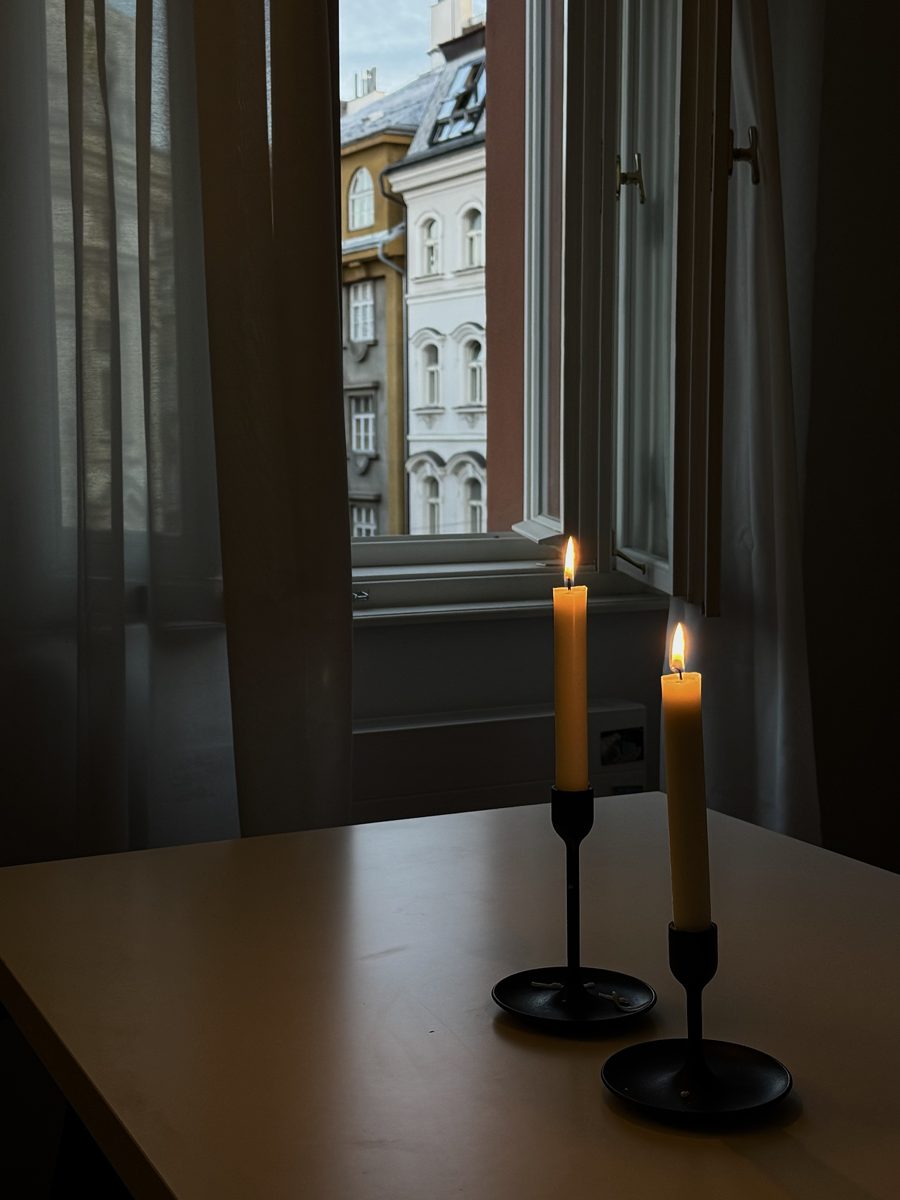 Two candles by an open window, Prague rooftops outside