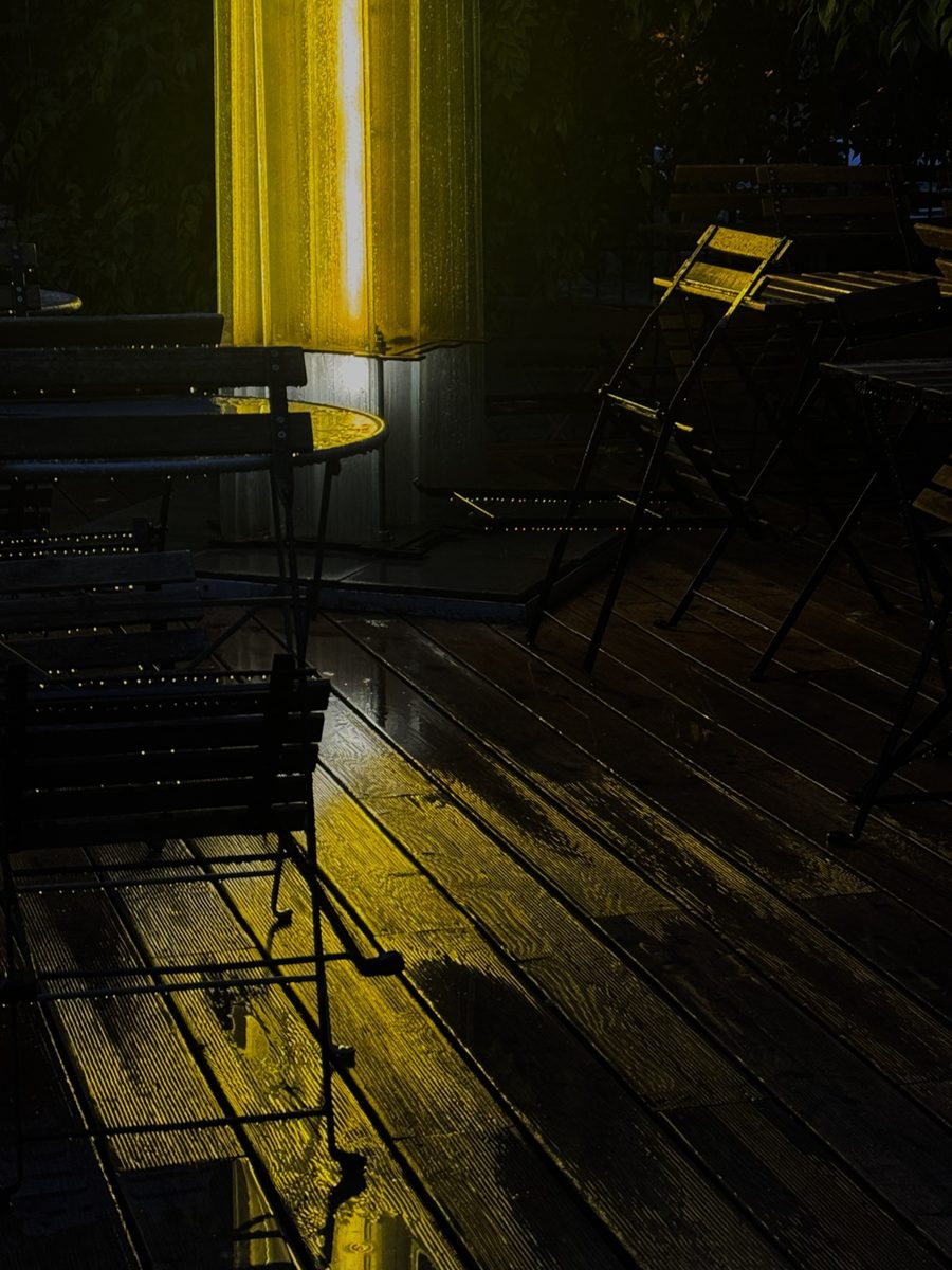 Rain on an empty café terrace, lit yellow