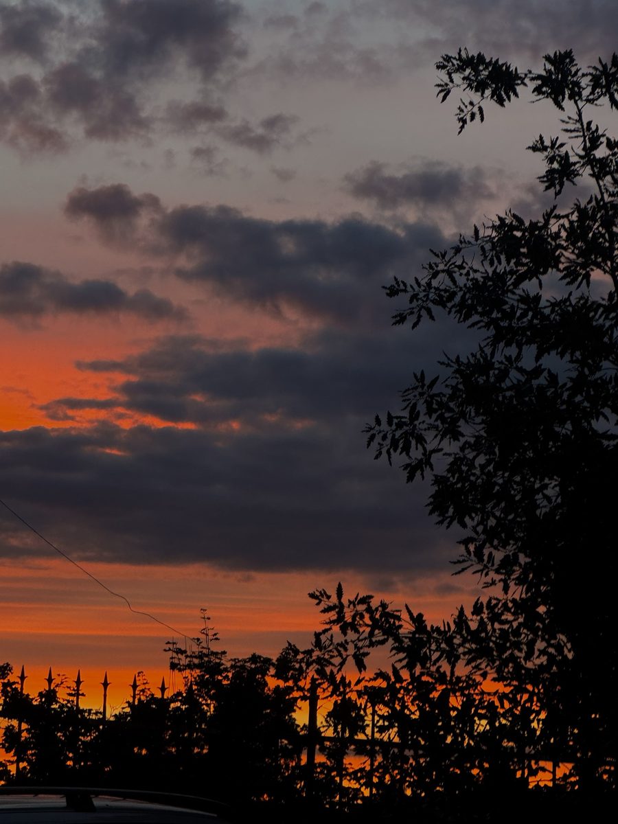 Orange sunset behind clouds and a fence