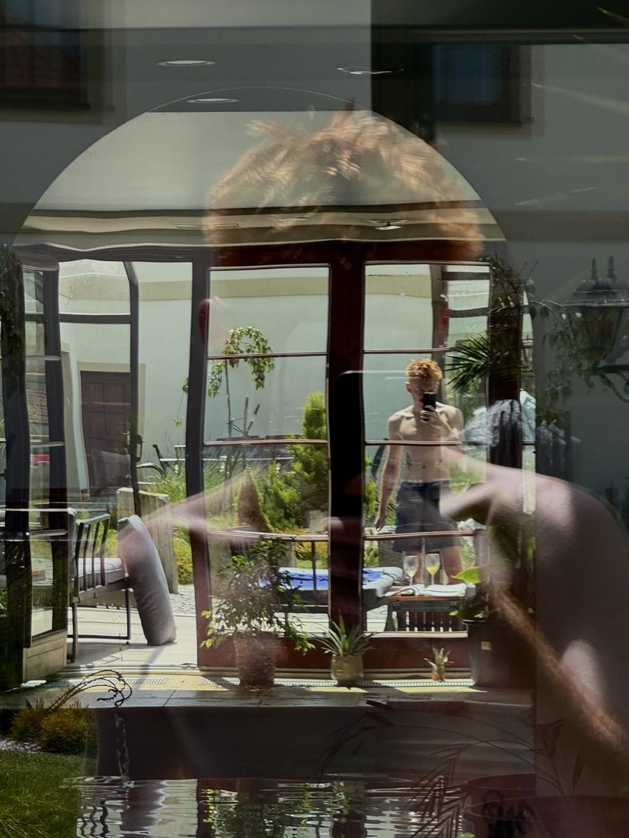 A shirtless mirror selfie, doubled in a window reflection